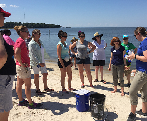 Group of people listening to someone speak on a beach.