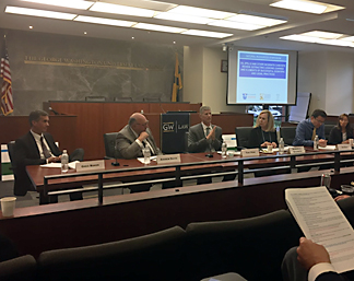 Men sitting at a table addressing a group.