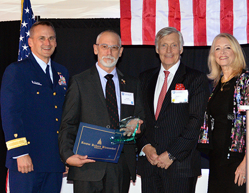 Four people posing for photo with an award in front of a flag.