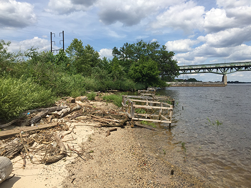 Riverbank with man-made cage-like device on the ground.