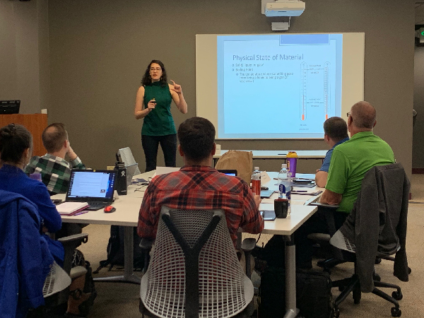 Woman leading a class, standing next to a screen.