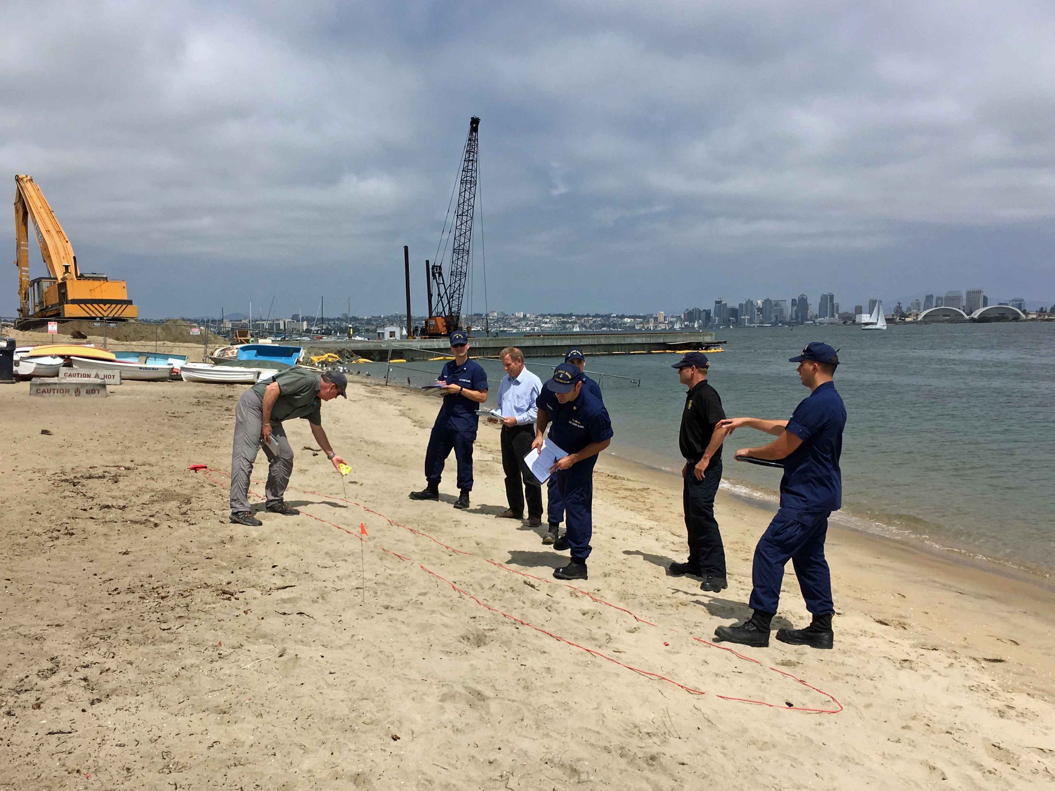 Instructor talking to several individuals in blue uniforms on a beach.