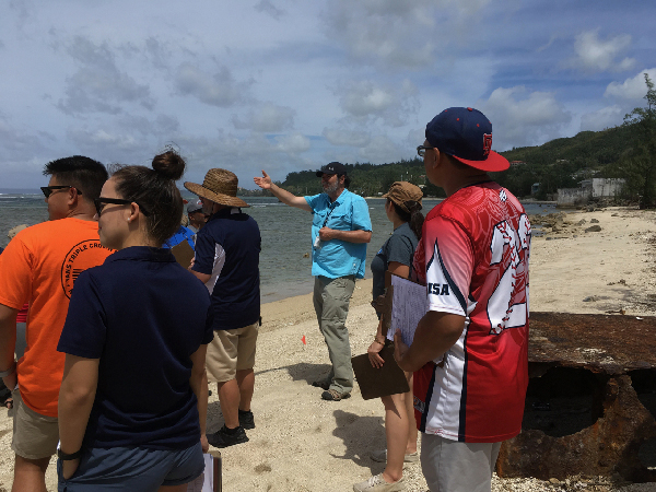 A group of people listening to an instructor on a beach.