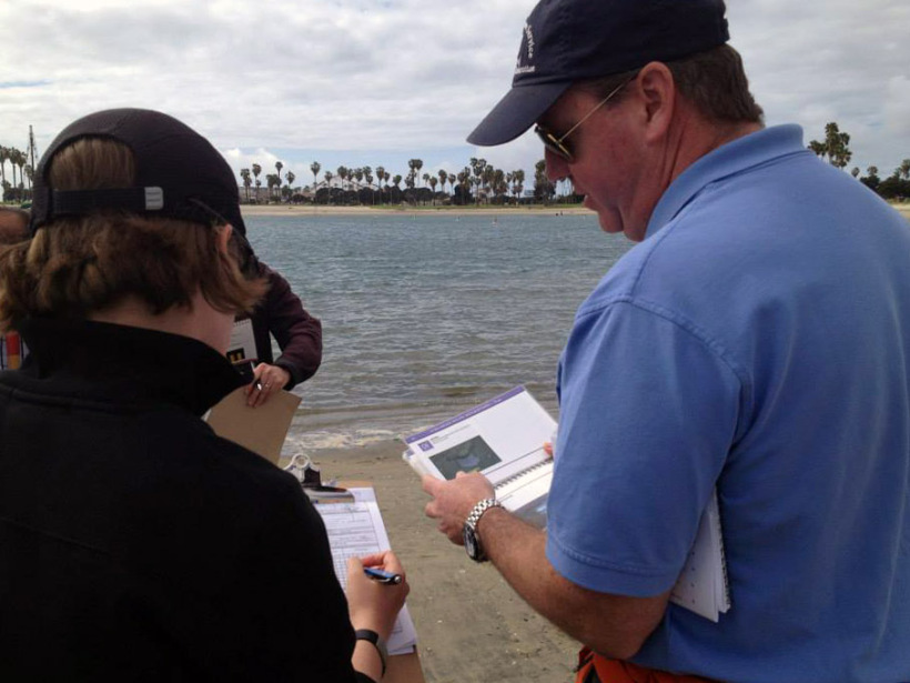 Two people on a shoreline looking at clipboards.