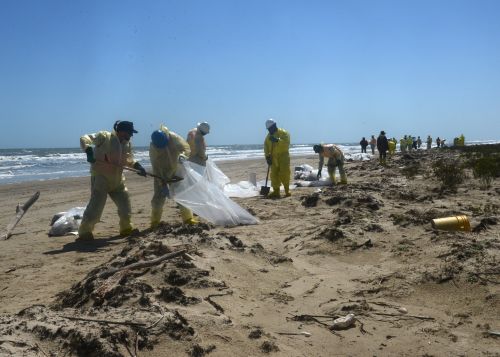 photo of people removing oil-contaminated sand from beach.