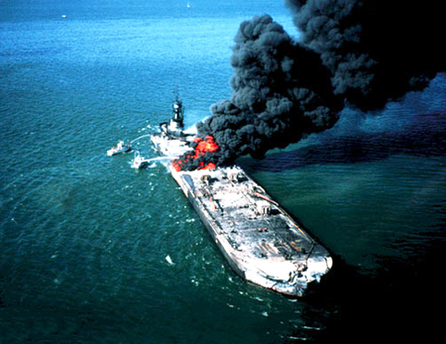 A barge on fire with black smoke pouring out.