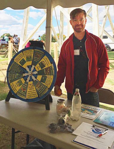 Man at a booth with large wheel (part of an educational game).