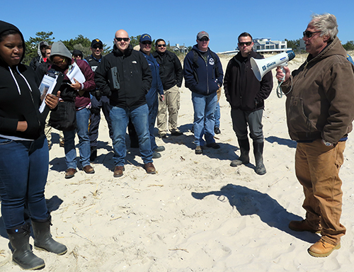 Man addresses group of students standing on a beach.