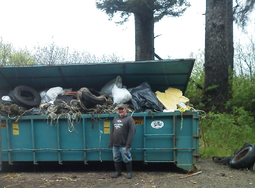 Man stands in front of full dumpster.