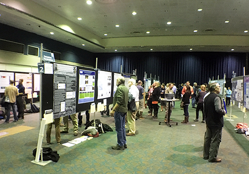 People standing in large hall looking at posters. 