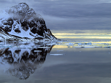Mountain surrounded by water with floating ice in Arctic Circle.