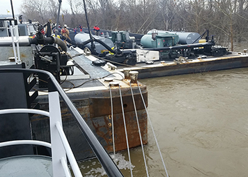 Workers on a river edge pump oil from a damaged barge.