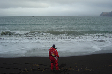 Coast Guard member stands on beach in front of ocean.
