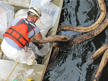 A worker removing oiled sorbent material from inside the cofferdam around ship