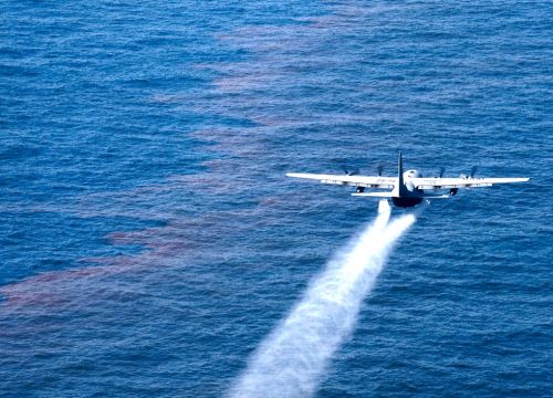 An Air Force plane drops an oil-dispersing chemical onto an oil slick on ocean.