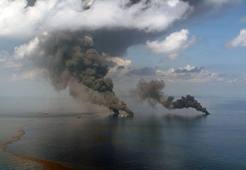 Plumes of smoke from two fires burning oil on the ocean surface.