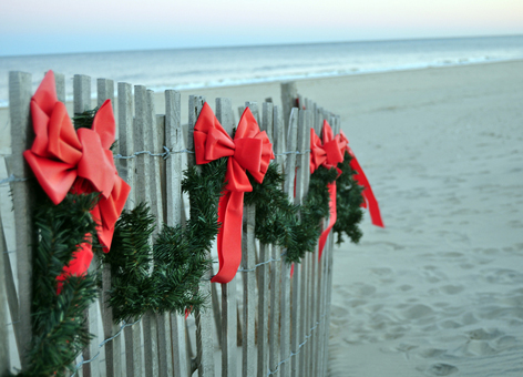 Red bows and evergreen bows on a fence on a beach.