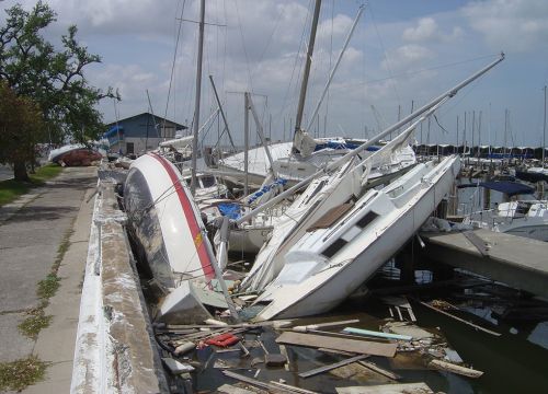 Wrecked sailboats and debris along a dock after a hurricane.