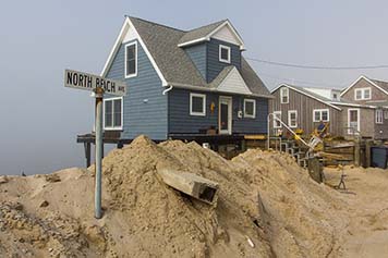 A street sign is buried under huge piles of sand in front of a beach community.