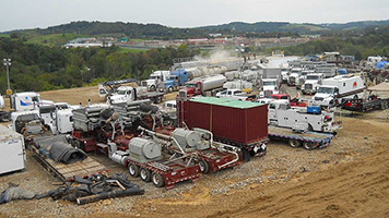 Trucks and heavy machinery used to drill for natural gas parked in dirt.