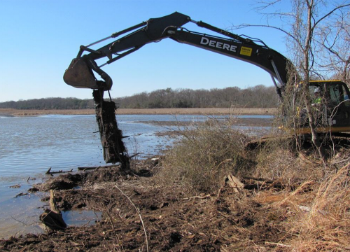 Excavator removes metal debris from the shore of a coastal landfill.