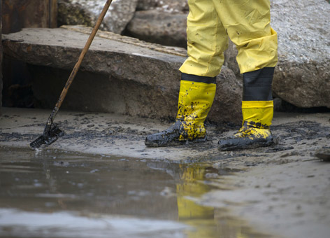 A cleanup worker uses a rake to gather oil on the shore of the Texas City Dike.