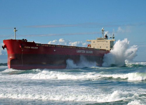 Large waves crash on a huge cargo ship aground on a beach. 