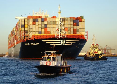 Huge container ship MSC Oscar being guided by two small ships into port.