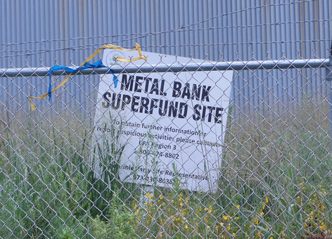 Sign behind a fence reading Metal Bank Super Fund Site.
