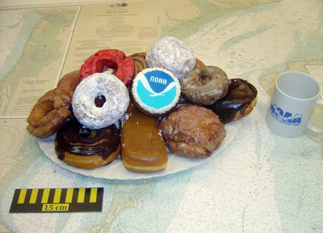 A mug, ruler & NOAA chart with a stack of donuts, one decorated with NOAA logo