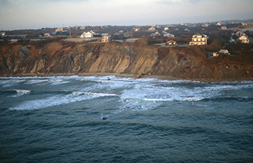 Houses on a cliff overlooking the ocean's pounding surf.