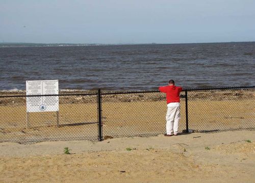 Person standing at a fenced-off beach closed to the public.