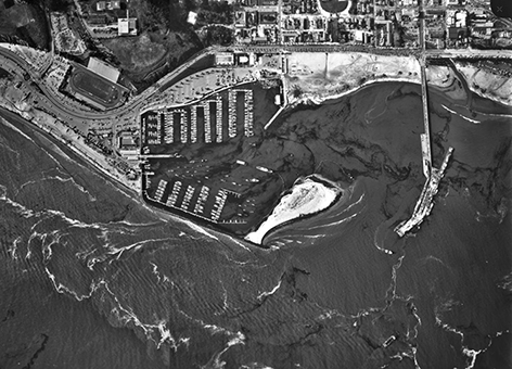 Aerial view of boats in a harbor with oil floating on the ocean.