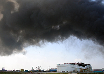 Smoke from the burning marsh blows over the damaged oil tank.