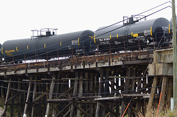 Tanker rail cars over a wood bridge.