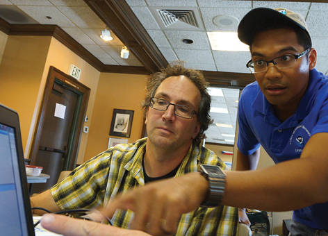 Man pointing at computer screen to another person.