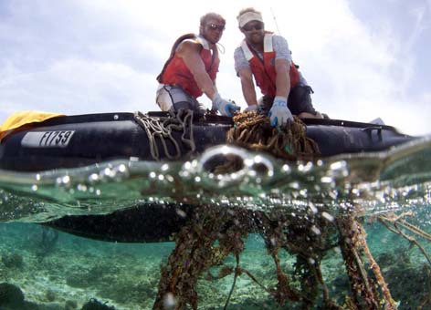 Two people pull a fishing net out of the water into a small boat.