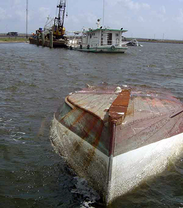 Overturned boat in water awaiting salvage with another boat salvaged nearby.