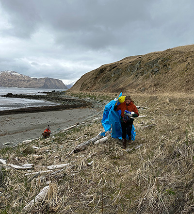 A photo of a participant carrying trash during a community marine debris cleanup in Humpy Cove, Unalaska, AK.