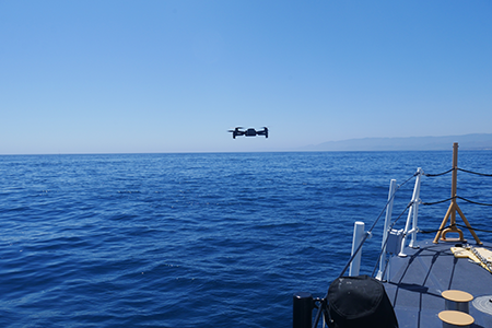 A small commercial off-the-shelf drone flying above water next to a vessel.