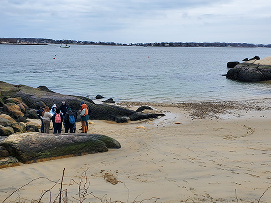A group of student trainees stand in a group along a Massachusetts shoreline.