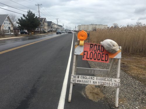 "Road Flooded" sign placed on the side of a road while cars pass by