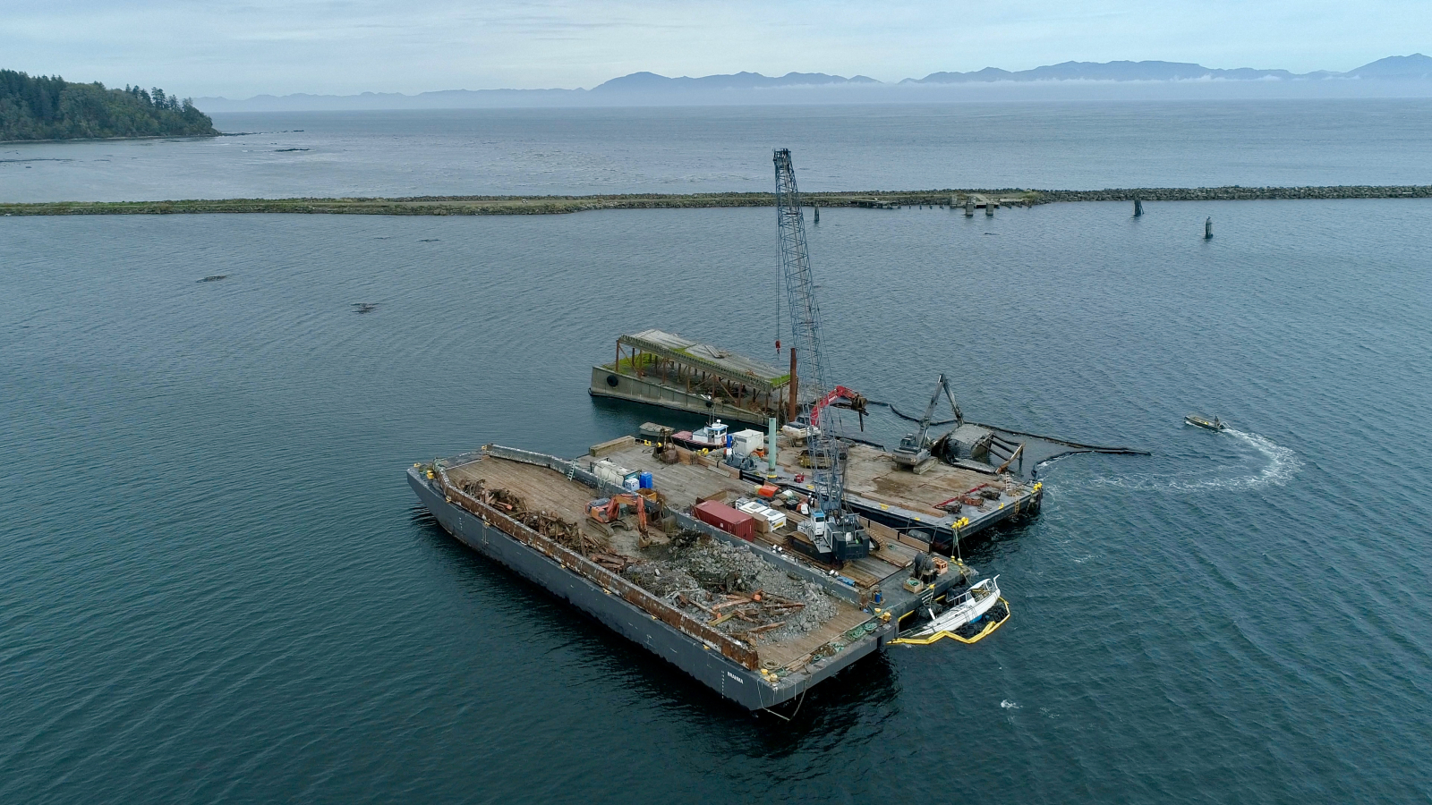 Three barges being used to remove a derelict bridge that sits in a bay.