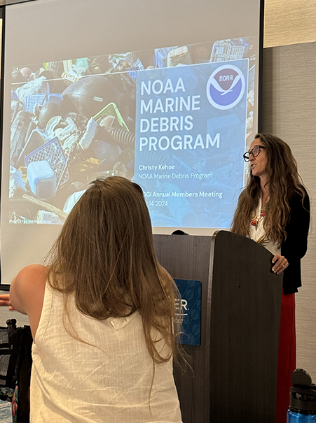 Women standing at podium giving presentation on federal marine debris program.