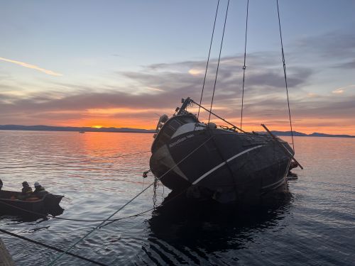 Fishing vessel rests on its side at the water's surface against a sunset backdrop.