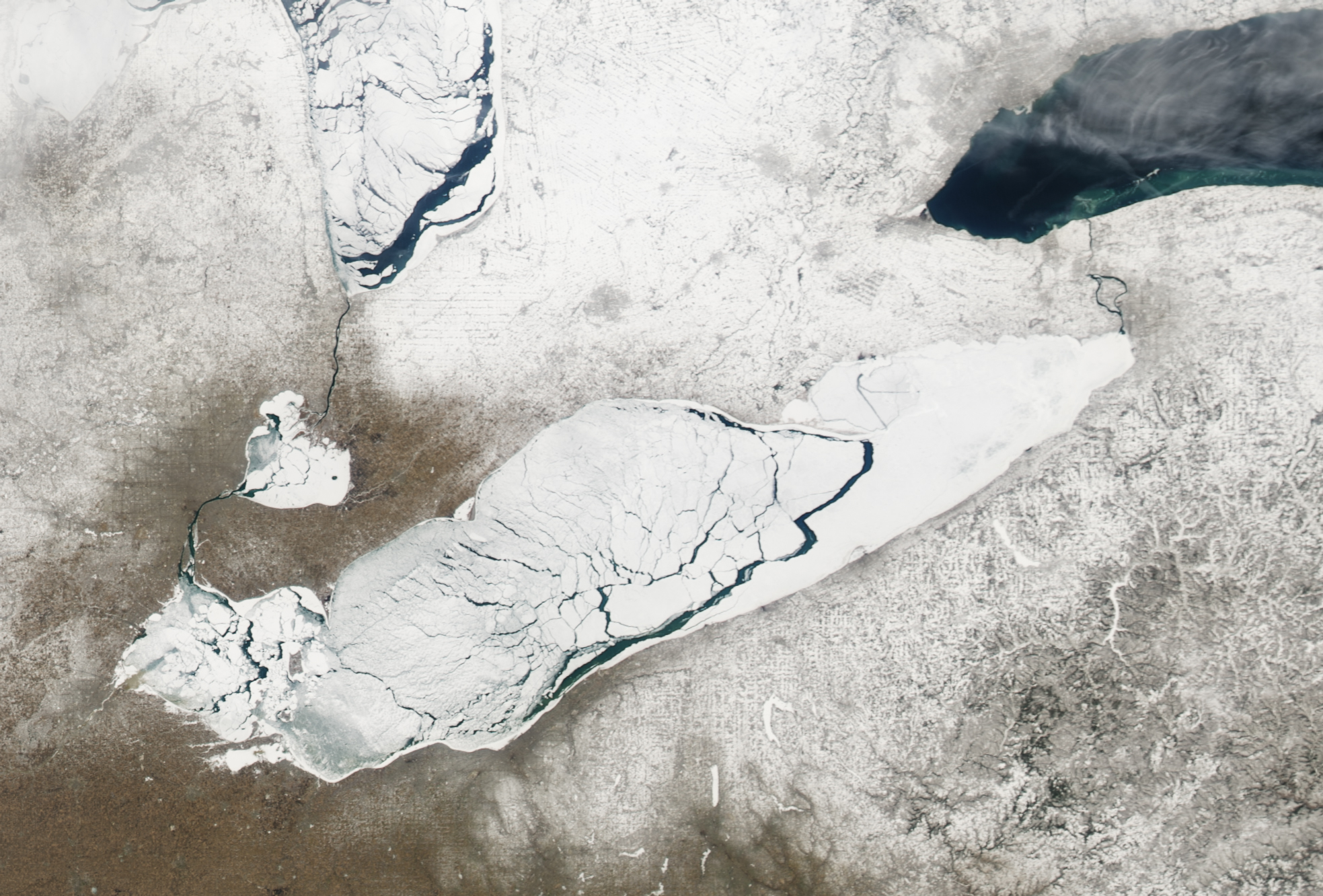 Satellite image of Lake Erie with ice almost completely covering the lake, but water peeks through large cracks stretching across the water body.