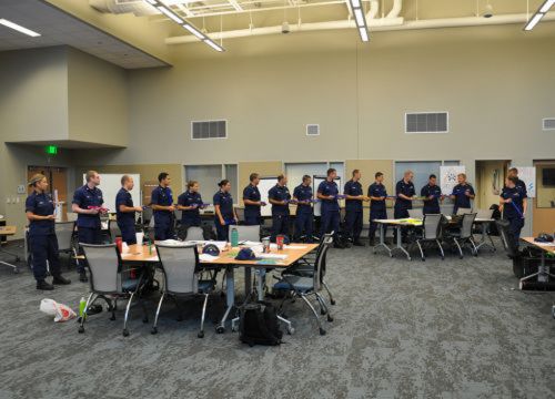 Students from the U.S. Coast Guard participate in a team-building exercise where they must rely on each other to achieve their common goal. (NOAA) Students from the U.S. Coast Guard stand in a line around a conference room.