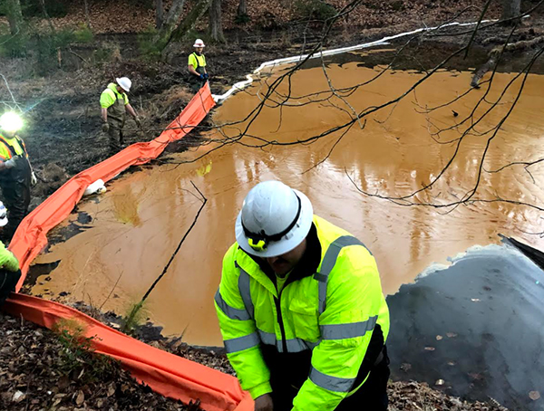 A spill response worker adjusts oil boom surrounding a large patch of oil on the water surface.