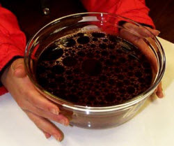 Dark blobs of oil float on water in a bowl.
