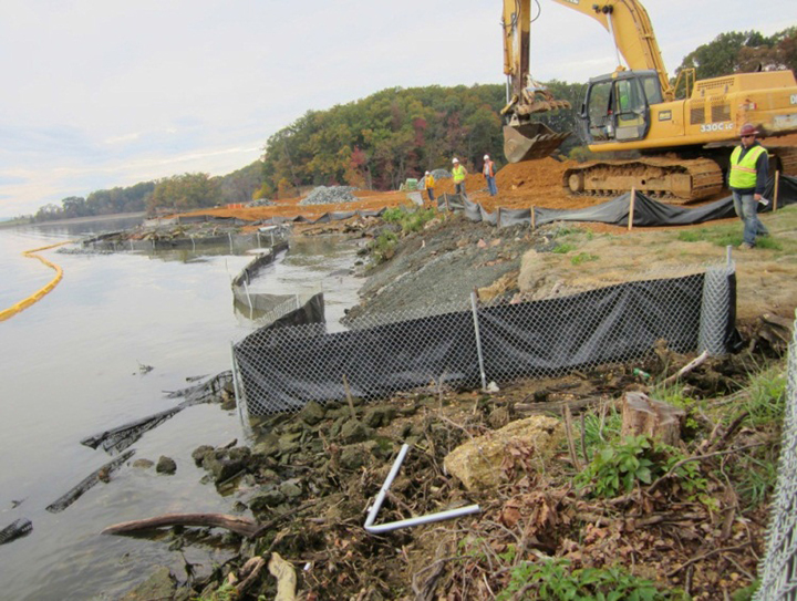 Construction workers oversee an excavator remaking a shoreline.